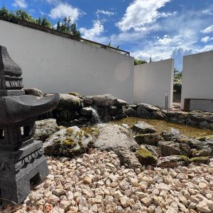 Estanque biológico con cascada de roca natural y muros blancos exentos en el Museo del Bonsái, diseñado por Espacio Acorde.