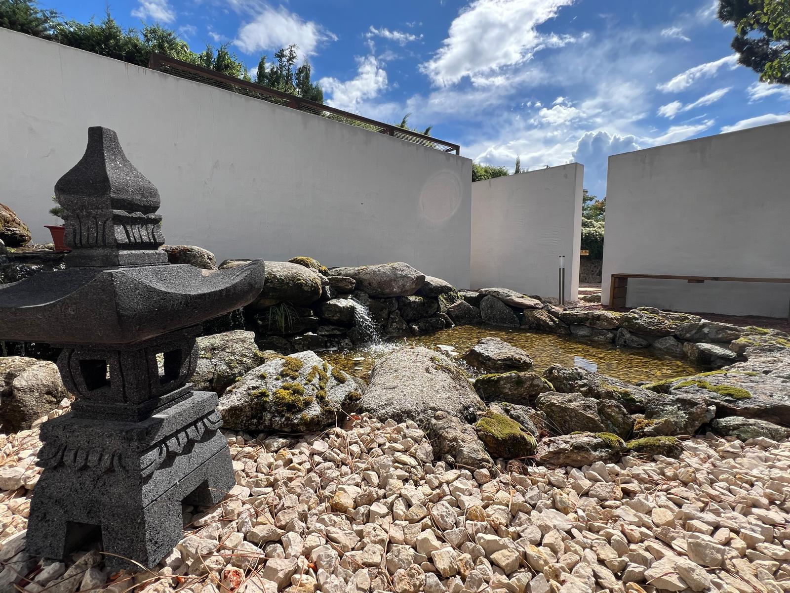 Estanque biológico con cascada de roca natural y muros blancos exentos en el Museo del Bonsái, diseñado por Espacio Acorde.