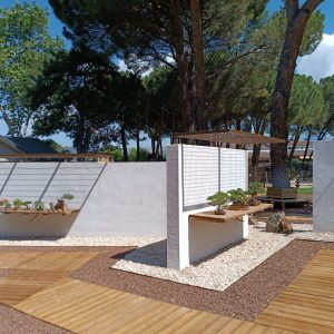 expositores de madera integrados en muros blancos sobre lecho de grava y pasarelas de madera en el Museo Municipal del Bonsái en Collado Villalba, diseñado por Espacio Acorde.