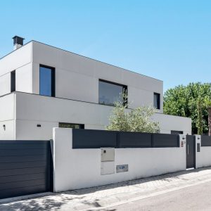 Vista en esquina de vivienda unifamiliar de obra nueva en Madrid de dos alturas, ventanas en aluminio gris grafito, vegetación integrada y muro perimetral.