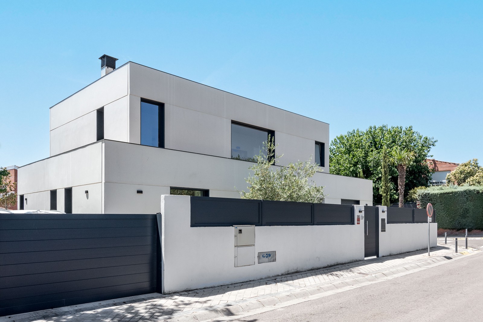 Vista en esquina de vivienda unifamiliar de obra nueva en Madrid de dos alturas, ventanas en aluminio gris grafito, vegetación integrada y muro perimetral.