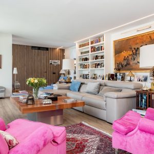 Vista panorámica de salón principal en vivienda unifamiliar de obra nueva en Madrid con panelado alistonado de madera, biblioteca a medida, iluminación LED perimetral y suelo radiante.