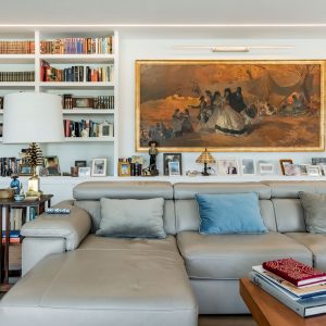 Zona de estar en salón de obra nueva en Madrid con biblioteca a medida integrada, iluminación LED perimetral, sofá gris, lienzo de gran formato y muebles clásicos.