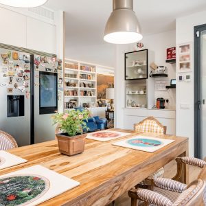 Vista de cocina y comedor de obra nueva en Madrid con mesa de madera maciza, electrodomésticos integrados, conexión directa al porche mediante gran ventanal y salón al fondo