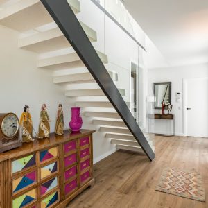 Vista de la estructura de escalera volada de obra nueva en Madrid con zanja metálica de acero, peldaños blancos, espacio aprovechado con mueble artesanal y frentes de armario de vidrio