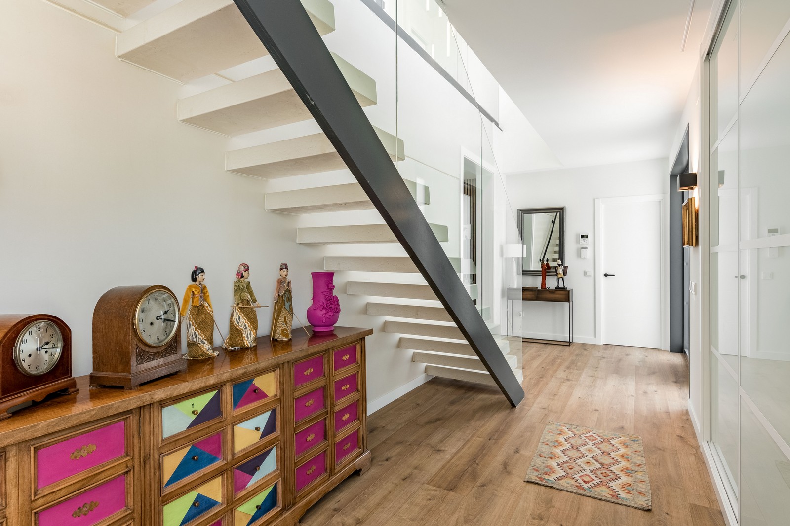 Vista de la estructura de escalera volada de obra nueva en Madrid con zanja metálica de acero, peldaños blancos, espacio aprovechado con mueble artesanal y frentes de armario de vidrio