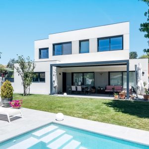 Vista panorámica del jardín, piscina privada y porche cubierto de una vivienda unifamiliar de obra nueva en Madrid por Espacio Acorde.