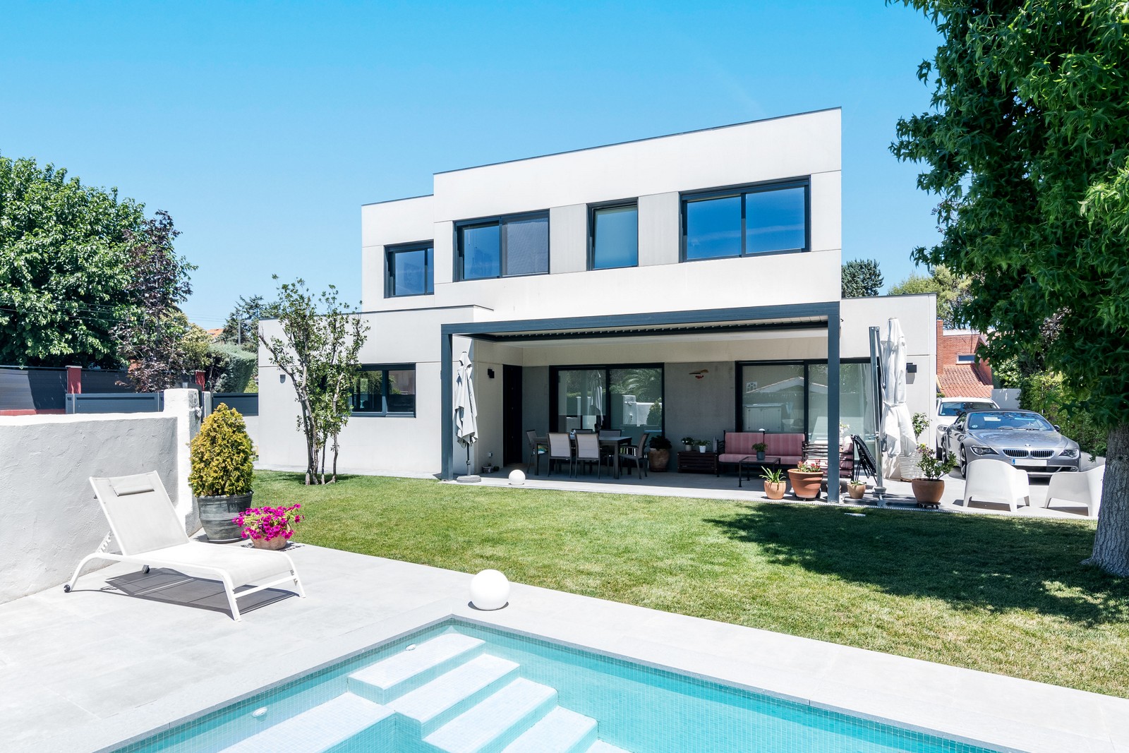 Vista panorámica del jardín, piscina privada y porche cubierto de una vivienda unifamiliar de obra nueva en Madrid por Espacio Acorde.