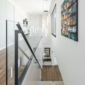 Recibidor de vivienda unifamiliar de obra nueva en Madrid con escalera volada blanca, armarios empotrados de vidrio translúcido y pavimento continuo.