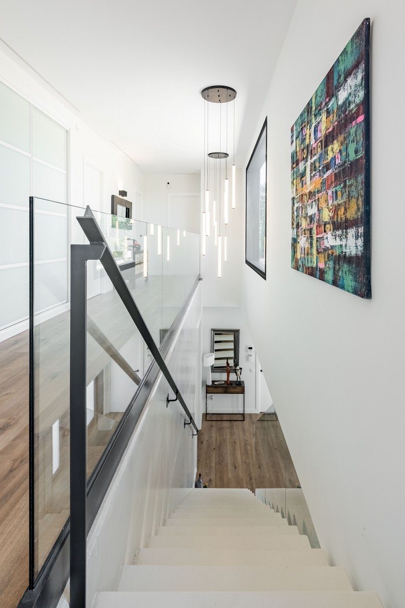 Recibidor de vivienda unifamiliar de obra nueva en Madrid con escalera volada blanca, armarios empotrados de vidrio translúcido y pavimento continuo.