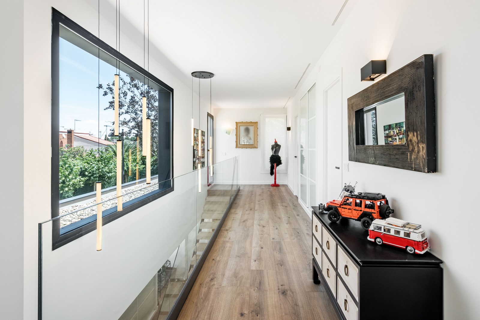 Distribuidor en doble altura de vivienda unifamiliar de obra nueva en Madrid con barandilla de vidrio, gran ventanal, lámparas suspendidas y pavimento continuo