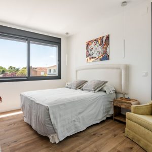 Dormitorio principal de obra nueva en Madrid con doble orientación solar, grandes ventanas de aluminio con rotura de puente térmico, suelo radiante continuo y mobiliario de madera natural.