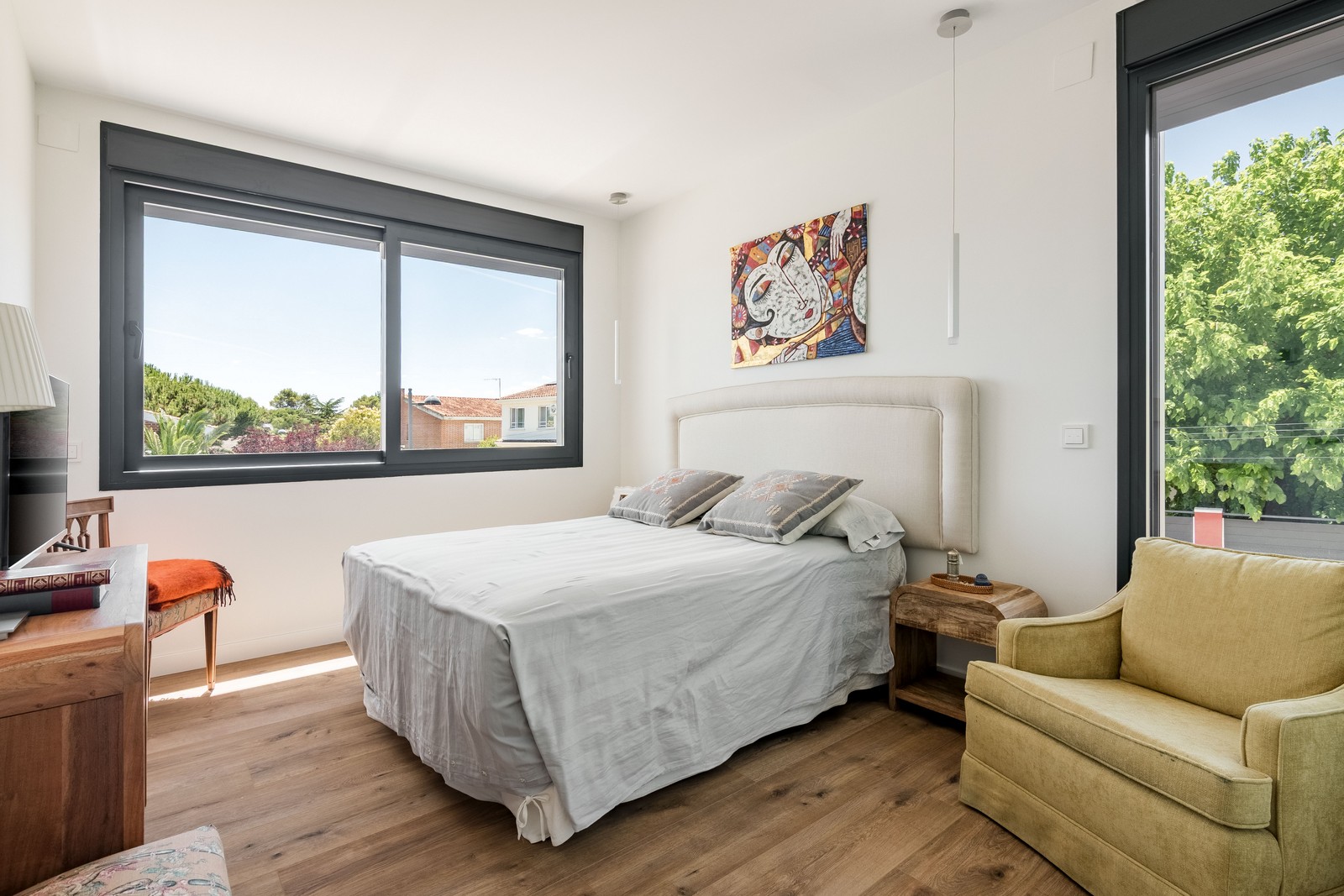 Dormitorio principal de obra nueva en Madrid con doble orientación solar, grandes ventanas de aluminio con rotura de puente térmico, suelo radiante continuo y mobiliario de madera natural.