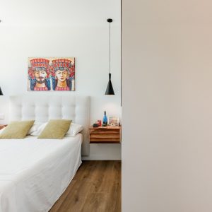 Diseño de dormitorio principal de obra nueva en Madrid, con mesillas suspendidas de madera natural, vestidor integrado con puertas correderas translúcidas y pavimento continuo.