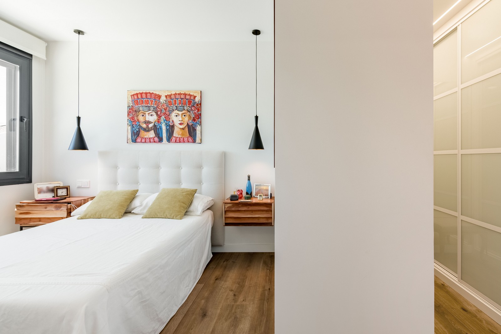 Diseño de dormitorio principal de obra nueva en Madrid, con mesillas suspendidas de madera natural, vestidor integrado con puertas correderas translúcidas y pavimento continuo.