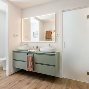 Diseño de baño para vivienda unifamiliar de nueva construcción en Madrid, con mueble verde salvia suspendido, doble lavabo de sobreponer y pavimento cerámico imitación madera.