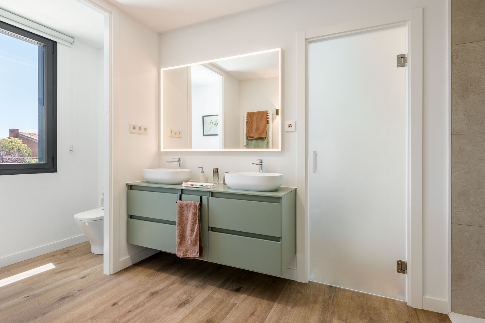 Diseño de baño para vivienda unifamiliar de nueva construcción en Madrid, con mueble verde salvia suspendido, doble lavabo de sobreponer y pavimento cerámico imitación madera.
