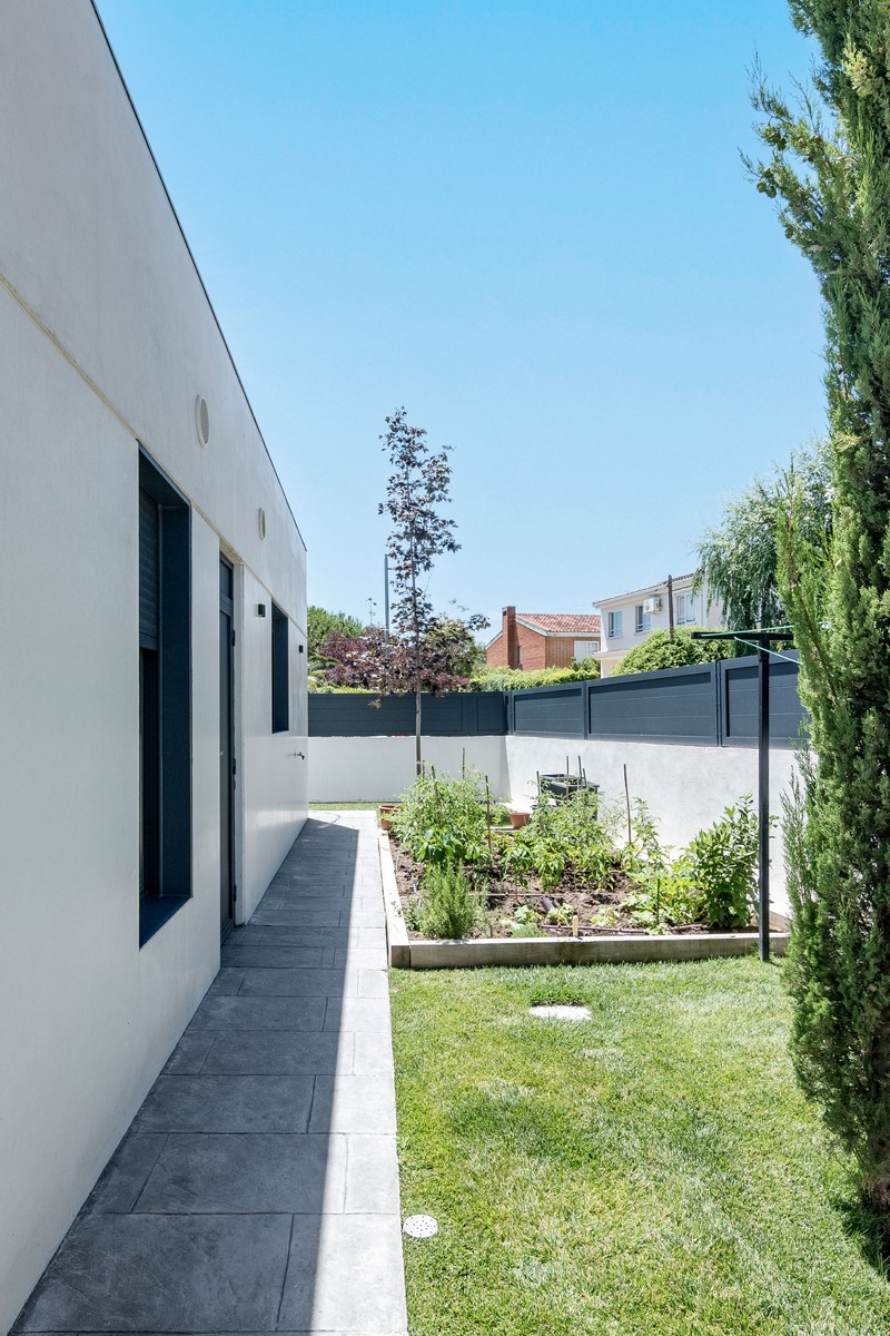 Vista del pasillo lateral y huerto urbano en bancal de madera en el jardín de una vivienda unifamiliar de obra nueva en Madrid por Espacio Acorde