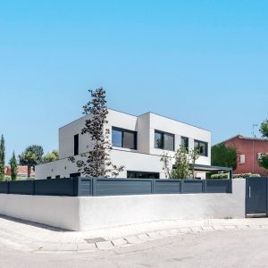 Vista de la fachada posterior y lateral de una vivienda unifamiliar de obra nueva en Madrid con porche, carpinterías gris grafito y cerramiento de parcela