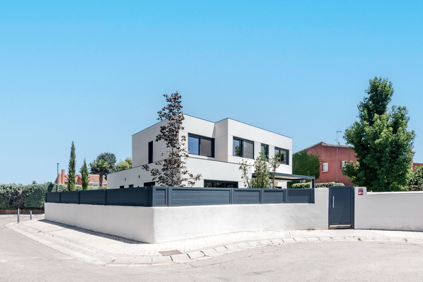 Vista de la fachada posterior y lateral de una vivienda unifamiliar de obra nueva en Madrid con porche, carpinterías gris grafito y cerramiento de parcela