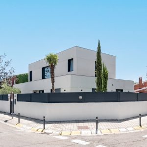 Vista en esquina de vivienda unifamiliar de obra nueva en Madrid de dos alturas, ventanas en aluminio gris grafito, vegetación integrada y muro perimetral.
