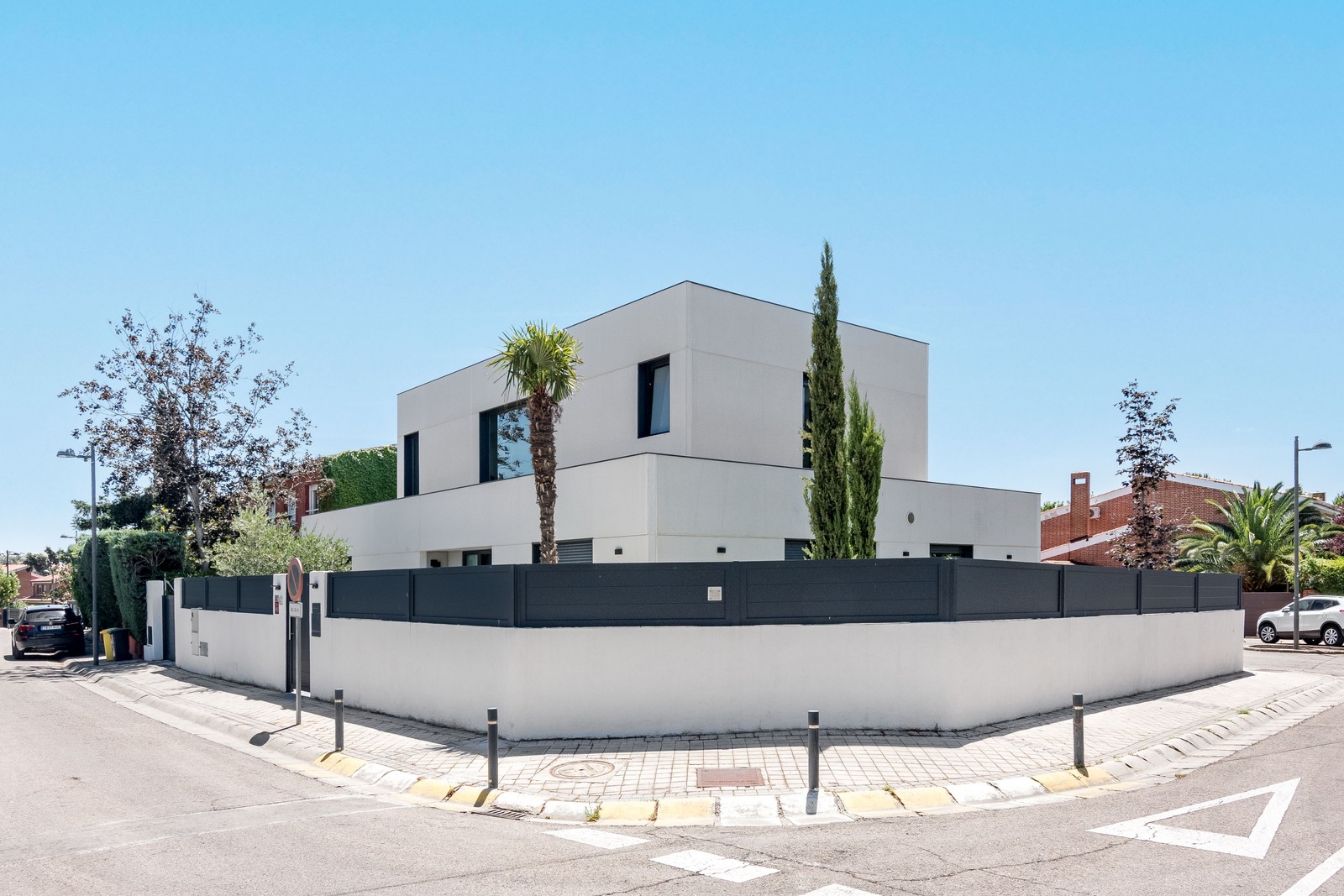 Vista en esquina de vivienda unifamiliar de obra nueva en Madrid de dos alturas, ventanas en aluminio gris grafito, vegetación integrada y muro perimetral.