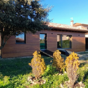 Fachada de vivienda unifamiliar de madera en Colmenarejo con revestimiento de madera natural y jardín, diseñada por estudio de arquitectura sostenible en Madrid.