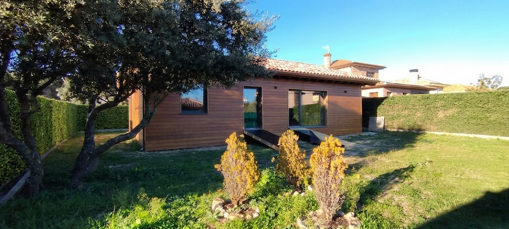 Fachada de vivienda unifamiliar de madera en Colmenarejo con revestimiento de madera natural y jardín, diseñada por estudio de arquitectura sostenible en Madrid.