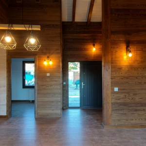 Recibidor y zonas de paso de casa de madera en Colmenarejo con paredes revestidas de madera natural y diseño de iluminación cálida con lámparas colgantes.