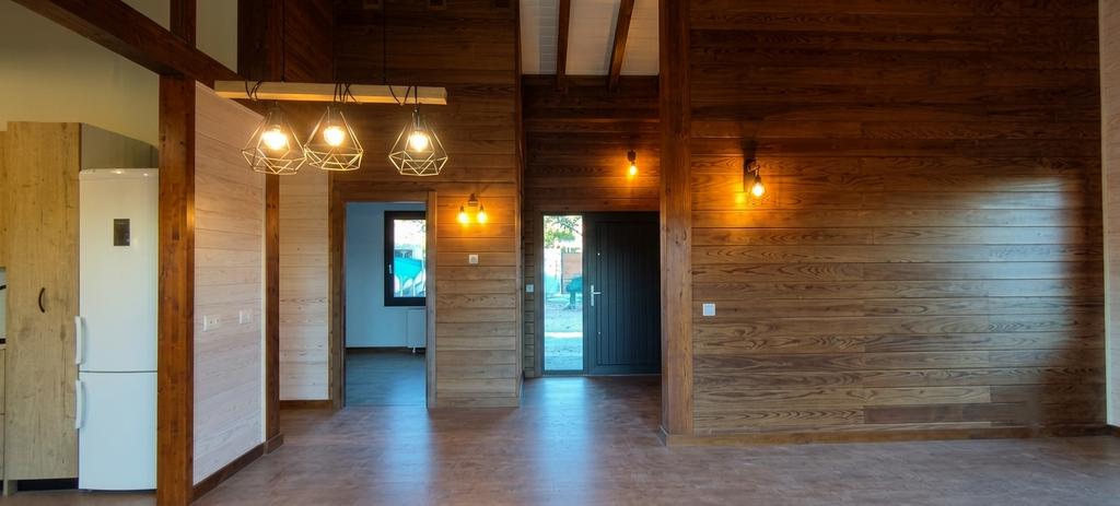Recibidor y zonas de paso de casa de madera en Colmenarejo con paredes revestidas de madera natural y diseño de iluminación cálida con lámparas colgantes.