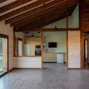 Interior luminoso de casa de madera en Colmenarejo con salón comedor de techos altos con vigas de madera vista y cocina semiabierta integrada.