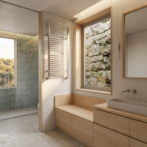 Baño suite perteneciente a la ampliación de una vivienda unifamiliar en Torrelodones, con mueble bajo y banco de madera clara, lavabo sobre encimera, radiador toallero, ventanal con vistas a muro de piedra y zona de ducha al fondo con alicatado cerámico verde verde agua, por Espacio Acorde.