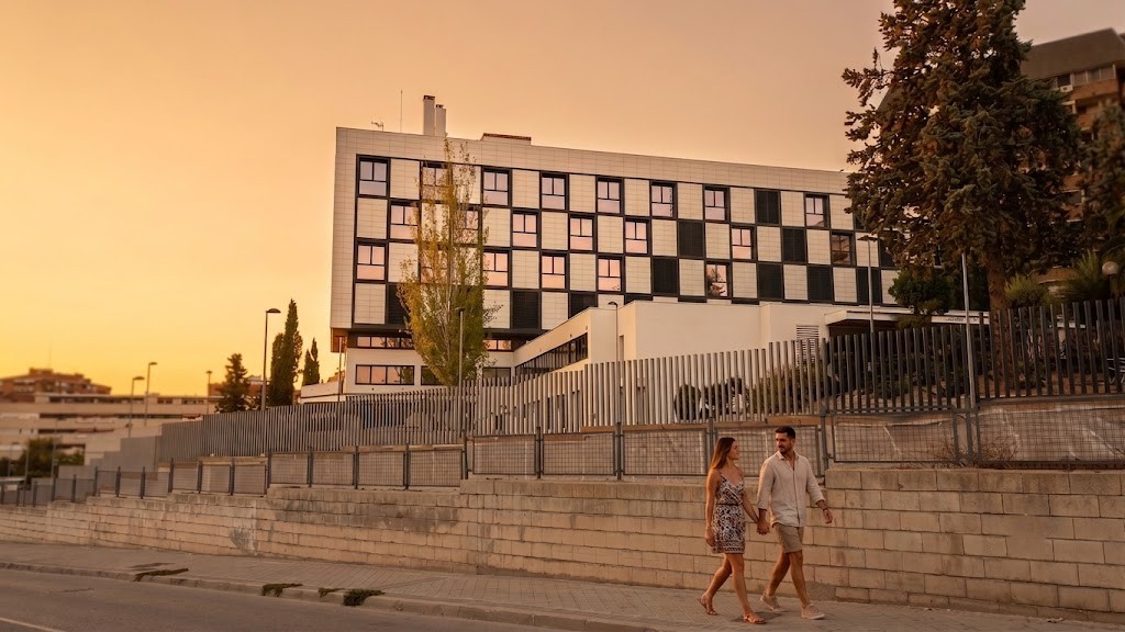 Vista exterior de la rehabilitación energética de la fachada modulada de la Clínica López Ibor al atardecer con personas paseando,