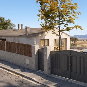 Vista exterior de una vivienda unifamiliar en la Sierra de Madrid, mostrando el muro perimetral de bloque, la puerta de acceso vehicular y peatonal, y un árbol central integrado en el diseño