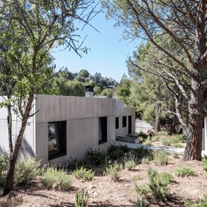 Vista de la arquitectura residencial integrada en una parcela con pendiente en Valdemorillo, mostrando los volúmenes grises de la vivienda unifamiliar aislada rodeada de pinos y vegetación autóctona de Madrid, diseñada por Espacio Acorde