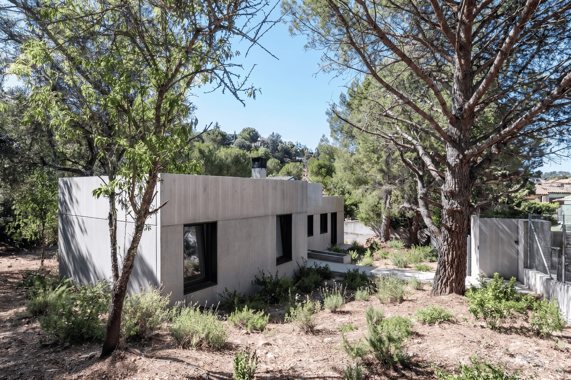Vista de la arquitectura residencial integrada en una parcela con pendiente en Valdemorillo, mostrando los volúmenes grises de la vivienda unifamiliar aislada rodeada de pinos y vegetación autóctona de Madrid, diseñada por Espacio Acorde