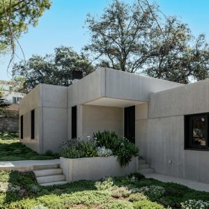Entrada principal de una vivienda unifamiliar prefabricada de hormigón en Madrid, mostrando un camino de acceso de hormigón y puerta oscura diseñado por Espacio Acorde.
