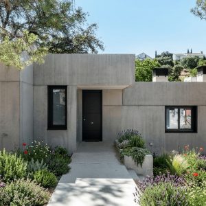 Fachada de acceso a vivienda unifamiliar de hormigón visto integrada en jardín, diseñada por Espacio Acorde, estudio de arquitectura en Madrid.