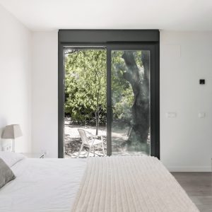 Vista interior de un dormitorio minimalista de diseño en Madrid, con un gran ventanal corredero que da acceso directo a un jardín, diseñado por Espacio Acorde.