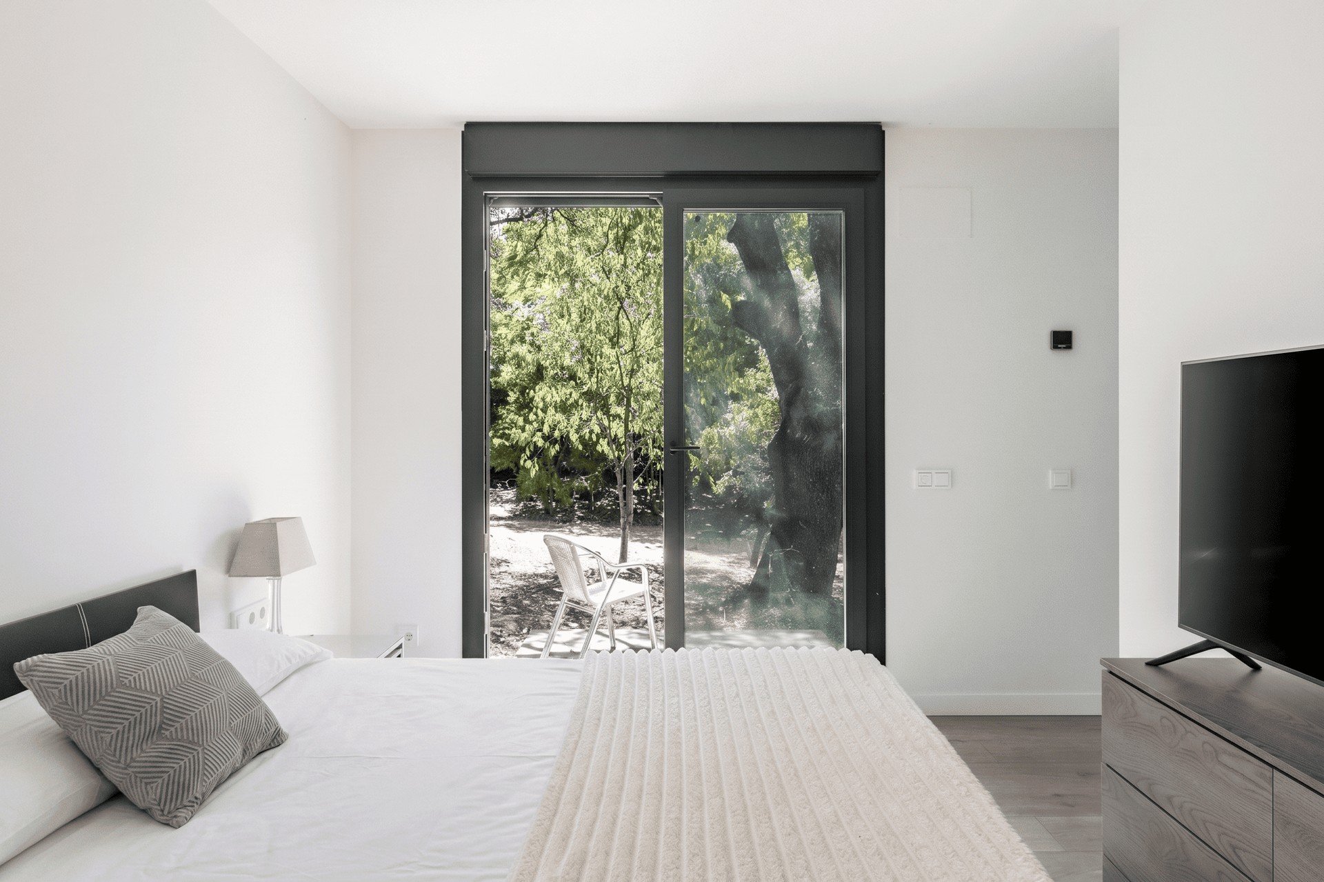 Vista interior de un dormitorio minimalista de diseño en Madrid, con un gran ventanal corredero que da acceso directo a un jardín, diseñado por Espacio Acorde.