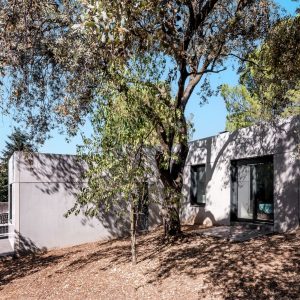 Fotografía de la fachada lateral de una vivienda unifamiliar prefabricada de hormigón en Madrid, mostrando la unión limpia de los paneles grises y las ventanas oscuras integradas, diseñada por Espacio Acorde