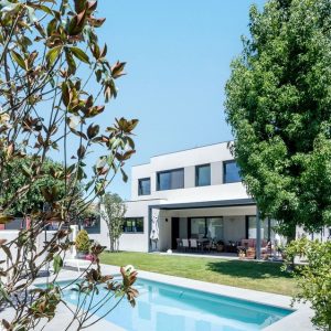 Enmarcado vegetal de la fachada posterior de una vivienda unifamiliar en Boadilla del Monte, con piscina rectangular, césped y arbolado maduro en parcela, por Espacio Acorde.