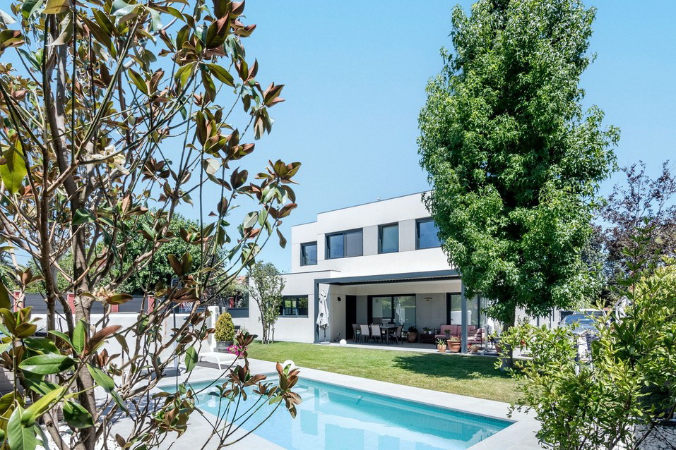 Enmarcado vegetal de la fachada posterior de una vivienda unifamiliar en Boadilla del Monte, con piscina rectangular, césped y arbolado maduro en parcela, por Espacio Acorde.