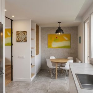 Fotografía de la zona de office en cocina reformada en Madrid, con mesa circular de madera, pared en textura gris, fregadero de acero inoxidable e iluminación natural desde terraza, por Espacio Acorde.