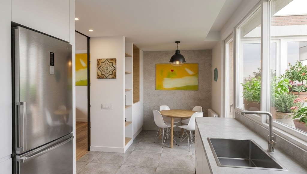 Fotografía de la zona de office en cocina reformada en Madrid, con mesa circular de madera, pared en textura gris, fregadero de acero inoxidable e iluminación natural desde terraza, por Espacio Acorde.